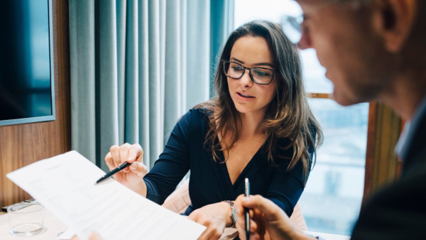 woman sitting at a desk pointing at a document with a pen