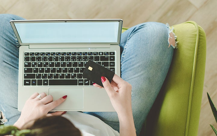 Persona utilizando un ordenador con una tarjeta de crédito en la mano