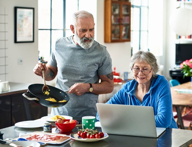 couple at kitchen counter with food looking at laptop