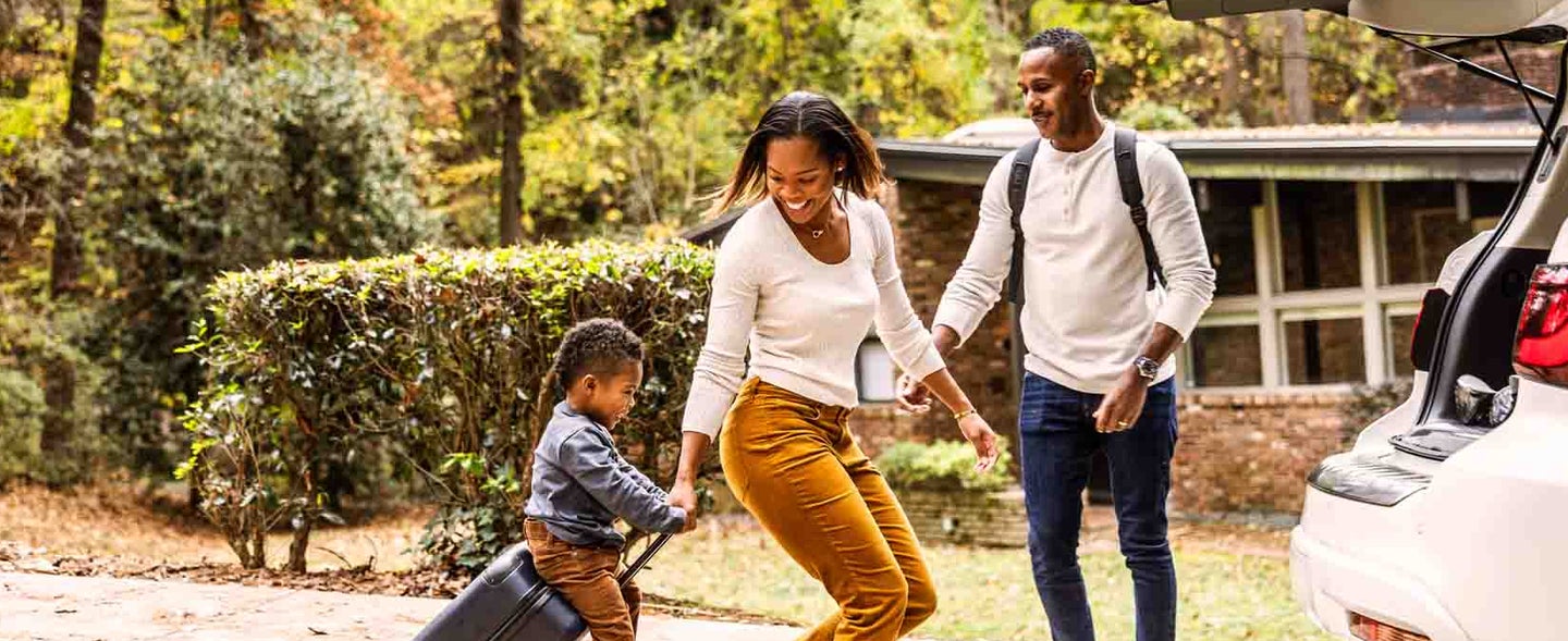 Family of three loading car with suitcase