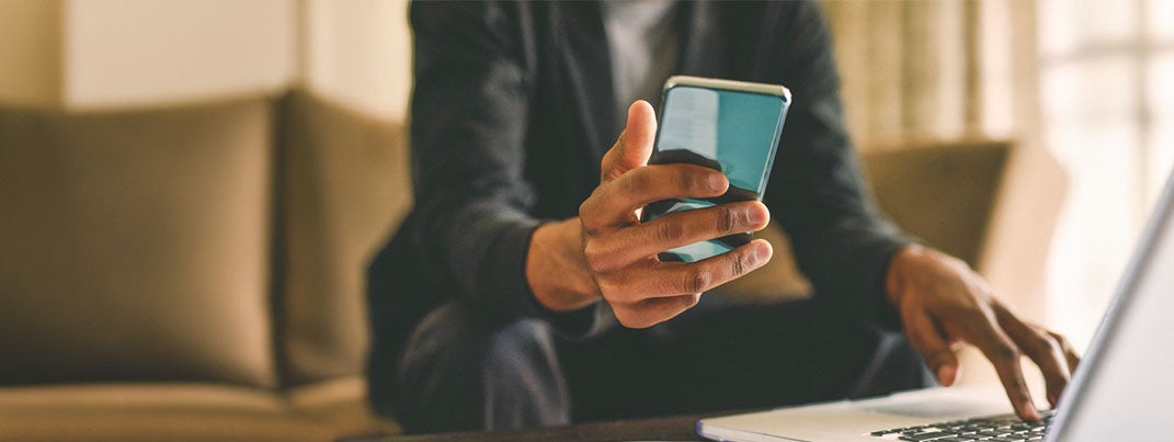 Man holding cellphone and using laptop