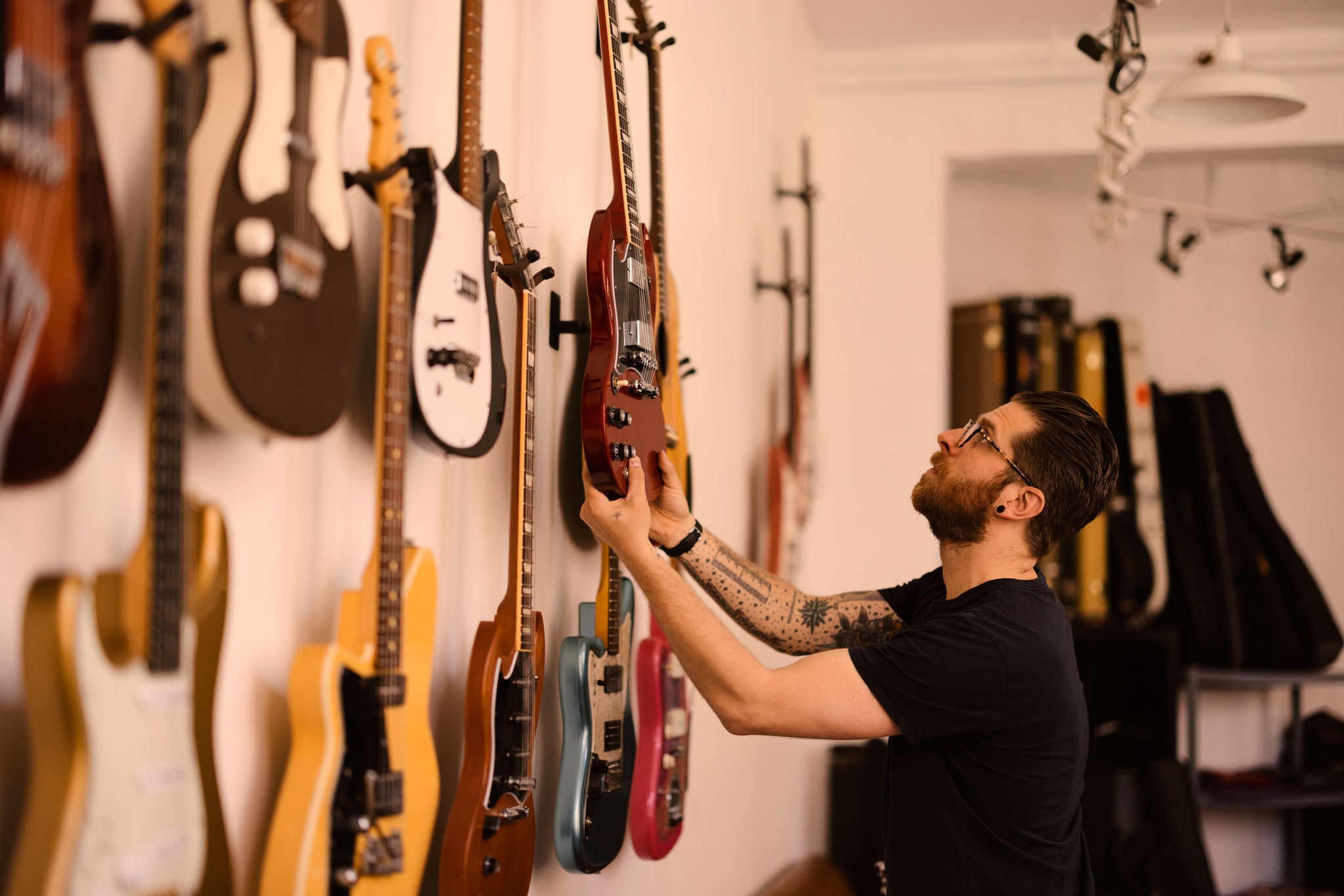 Ein Mann betrachtet diverse Gitarren, die an einer Wand hängen