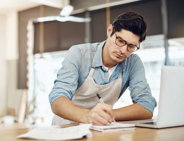 Man writing on notepad next to laptop
