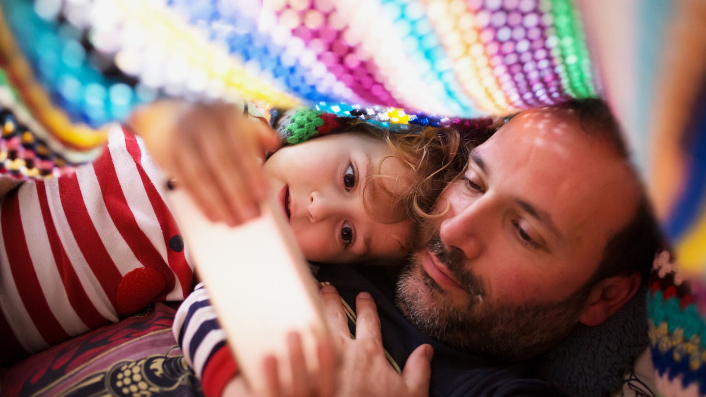 Father and daughter under a blanking looking at phone
