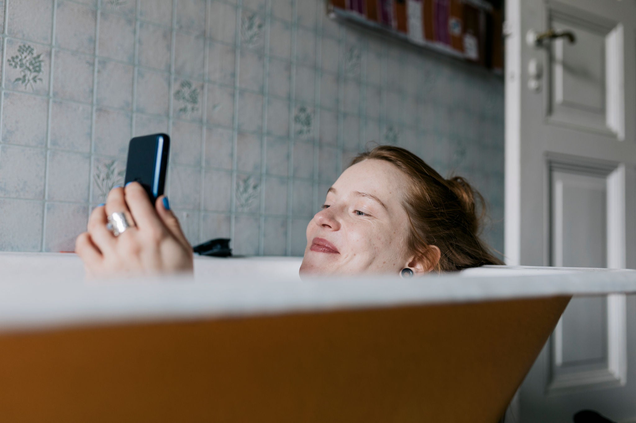 Frau liegt mit Handy in der Badewanne